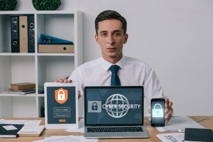 portrait of businessman showing laptop, tablet and smartphone with cyber security signs on screens